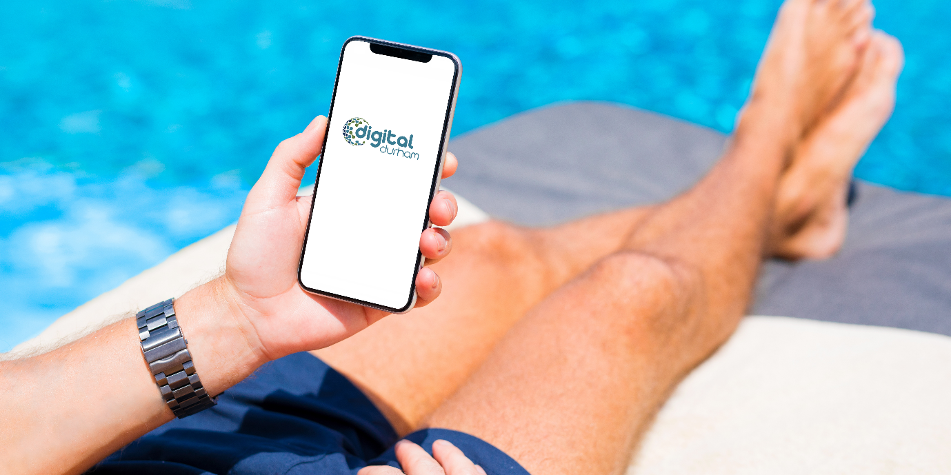 Man on sunlounger using mobile phone, next to a swimming pool.