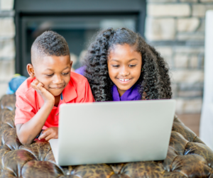 2 children laying in front of a laptop looking at the screen together 