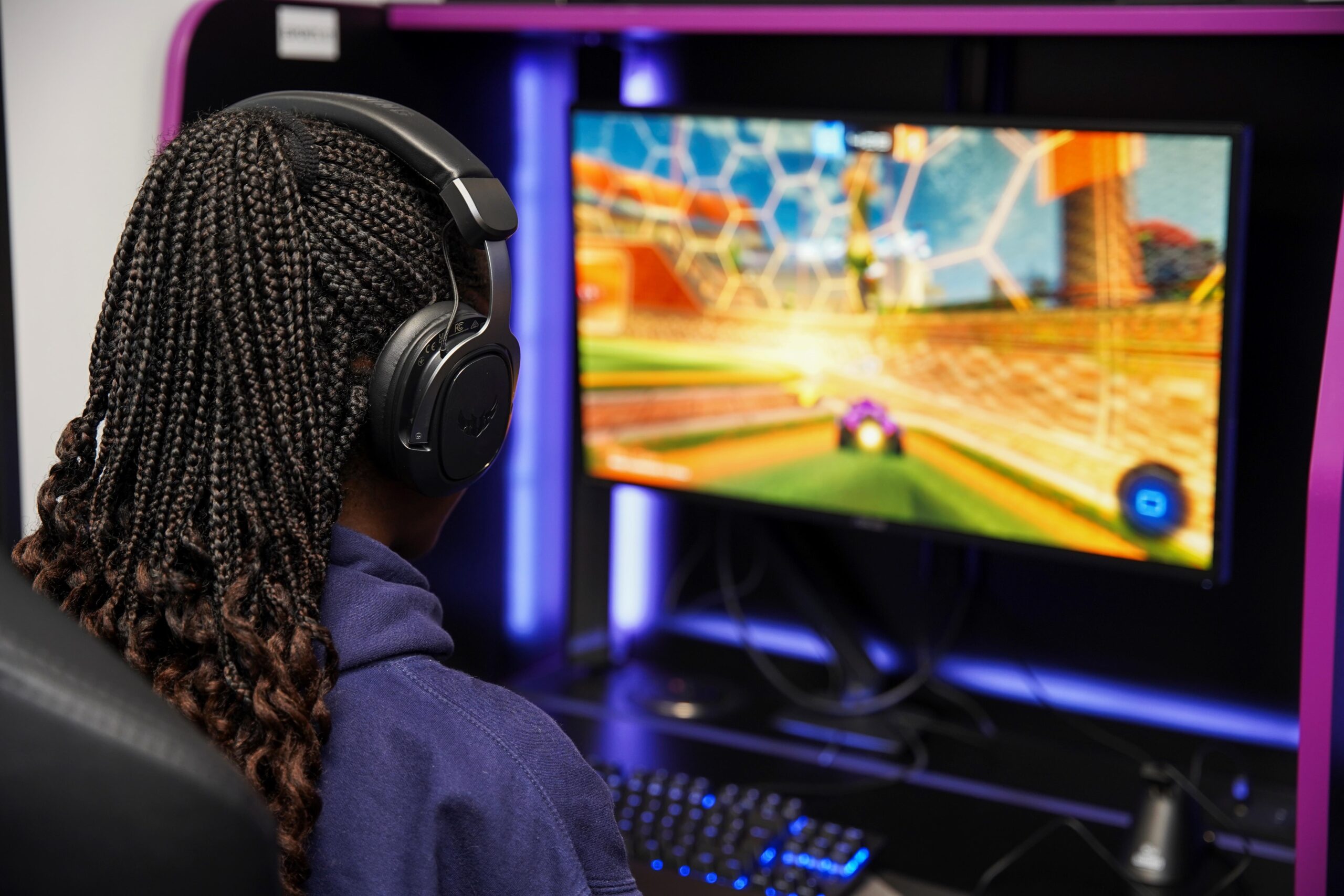 Girl sat in front of computer monitor, wearing headphones while playing a game.